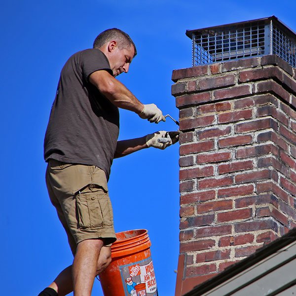 A man works on a chimney, using a bucket for brick pointing repairs.