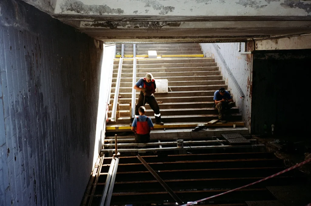 Three workers in safety vests take a break on stairs inside a partially constructed or renovated underground passageway, highlighting the importance of emergency repairs and safety measures​ to address DOB violations.