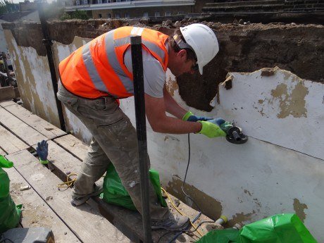 Construction worker in safety vest and hard hat grinds concrete wall with angle grinder.