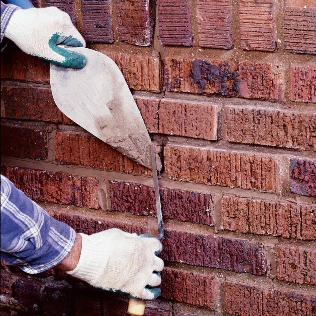 A person using a tool to cut into a brick wall, focusing on brick pointing for repair or restoration work.