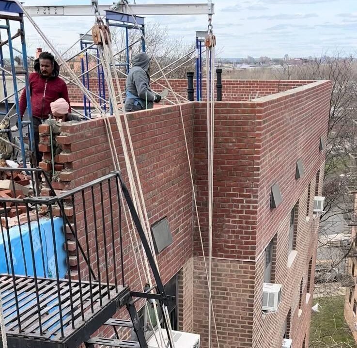 A crane lifts a blue tarp over a building where a team is performing brick pointing in NYC.