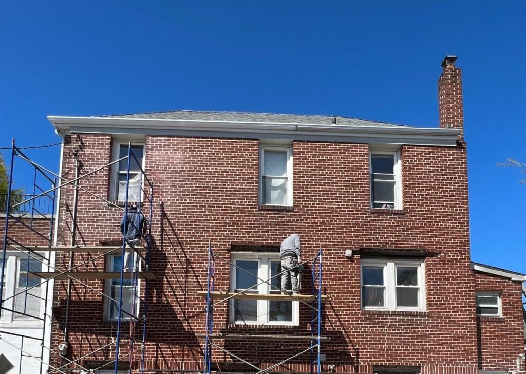 Worker on scaffolding repointing bricks on Brooklyn brownstone chimney repair.